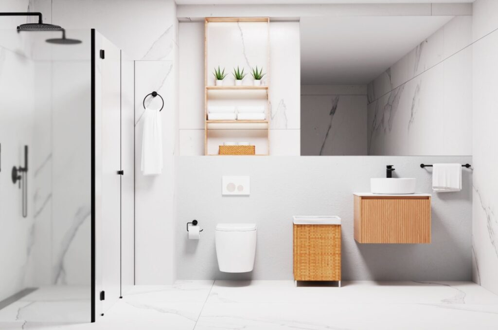 A modern bathroom featuring a minimalistic design with white marble walls and floor. The space includes a walk-in shower with a black showerhead, a floating wooden vanity with a round white sink, and a small wooden storage unit. A black towel rail and a toilet paper holder complement the sleek decor, while neatly stacked towels and small plants add a touch of warmth and greenery.